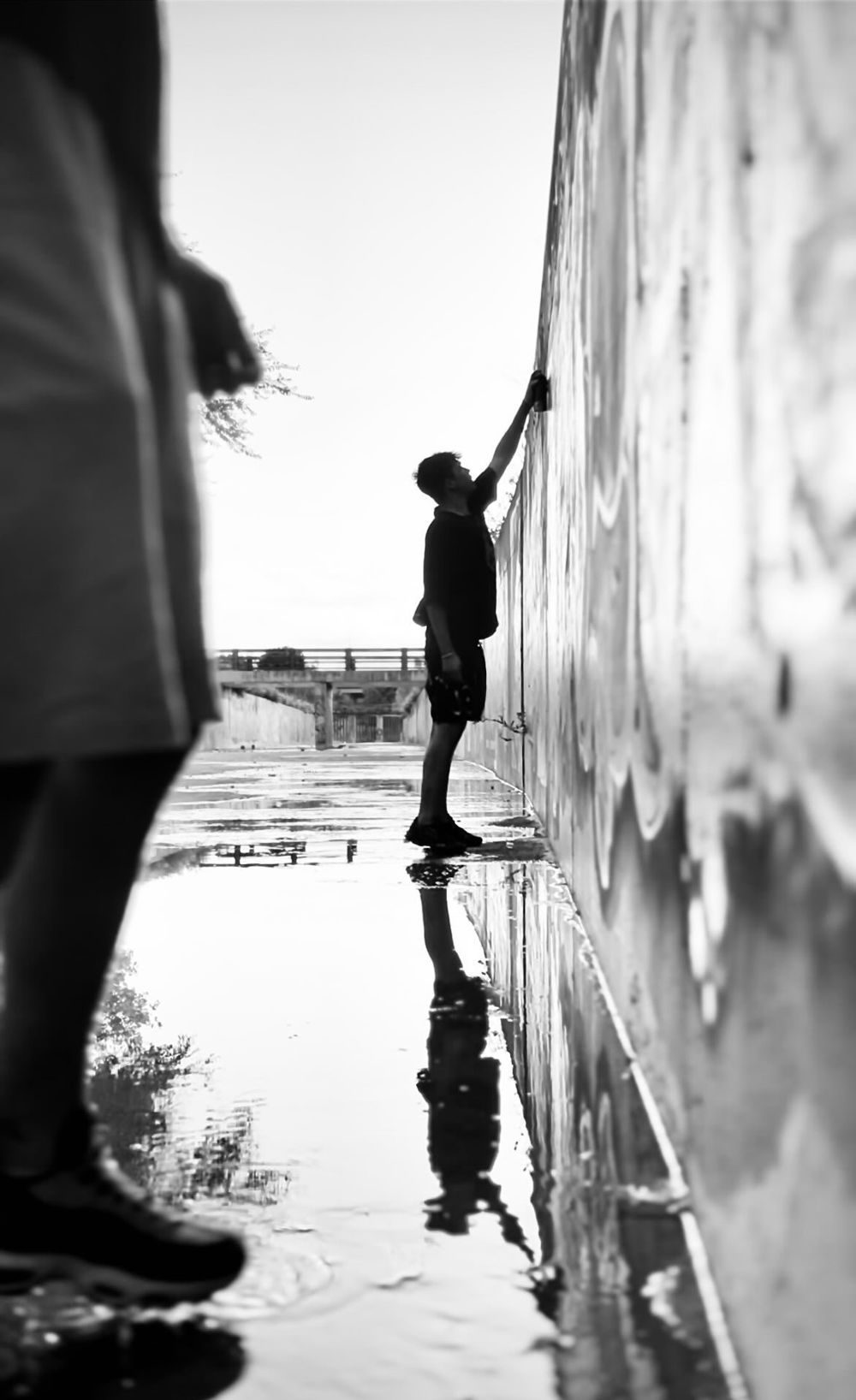 Maüro pintando una pared junto a un charco, en blanco y negro