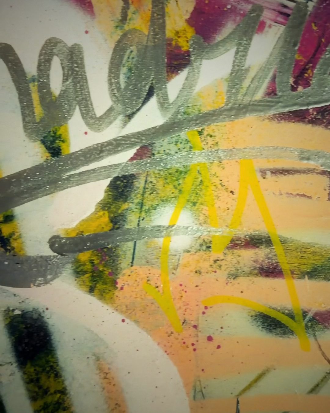 Detalle de un lienzo de Maüro: letras plateadas sobre spray amarillo, verde y rosa